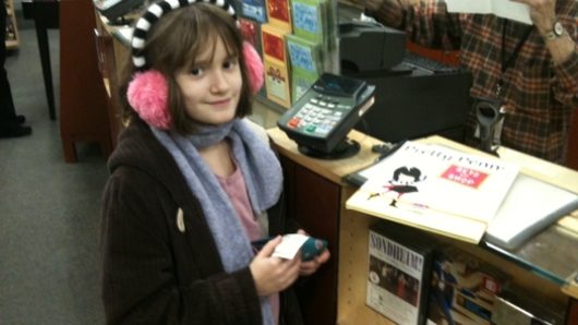 A photo of a girl wearing pink ear covers while siting at a magazine shop.
