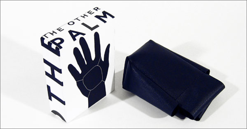 A design of a white box with a black hand and the text: The Other Palm. Near the box there is a blue leather bag.