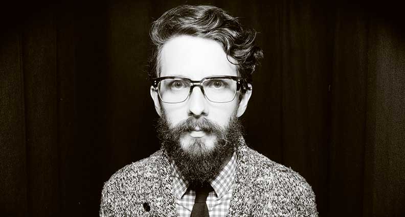 A black and white photo of a man wearing glasses, a tie and a checkered shirt.