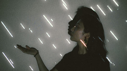 A photo of two girls seen from a side and holding a palm while some illuminated white lines fall like rain.