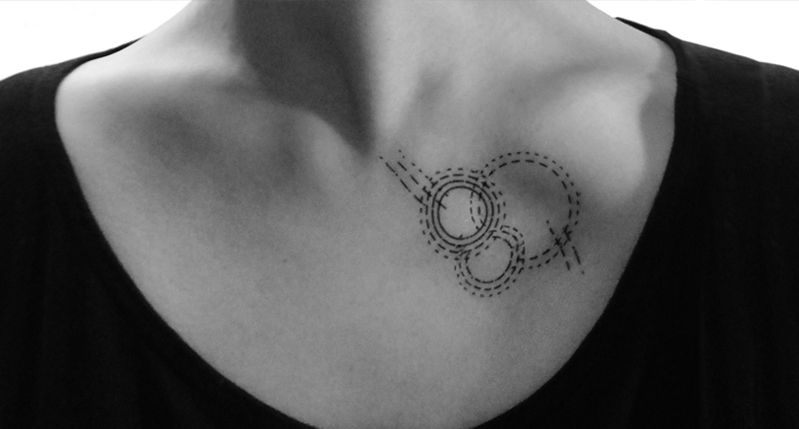 A black and white photo of a person's neck with a tattoo of three circles and some lines coming from them.