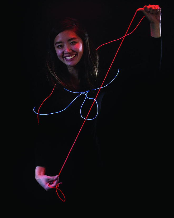A girl with a blue glowing wire around her that holds a red wire in her hands.