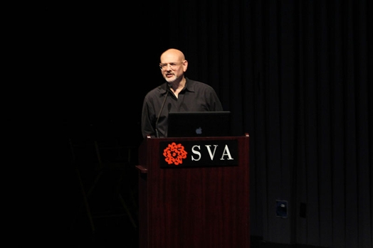 A photo of a man giving a lecture at a stand with SVA logo on it.
