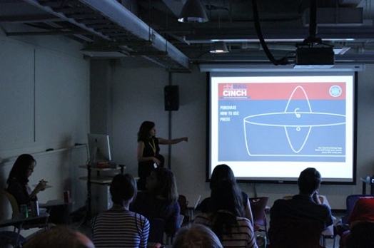 A photo of a woman giving a lecture to a class while showing a blueprint on a screen projector.