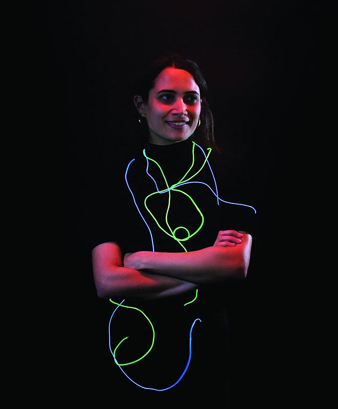 A smiling girl with green and blue glowing wires around her.