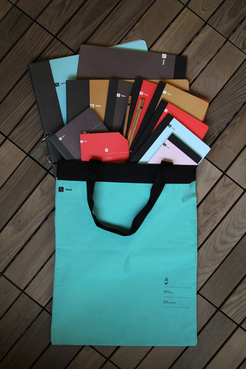 A photo of a cyan bag filled with different notebook cover designs and crayons.