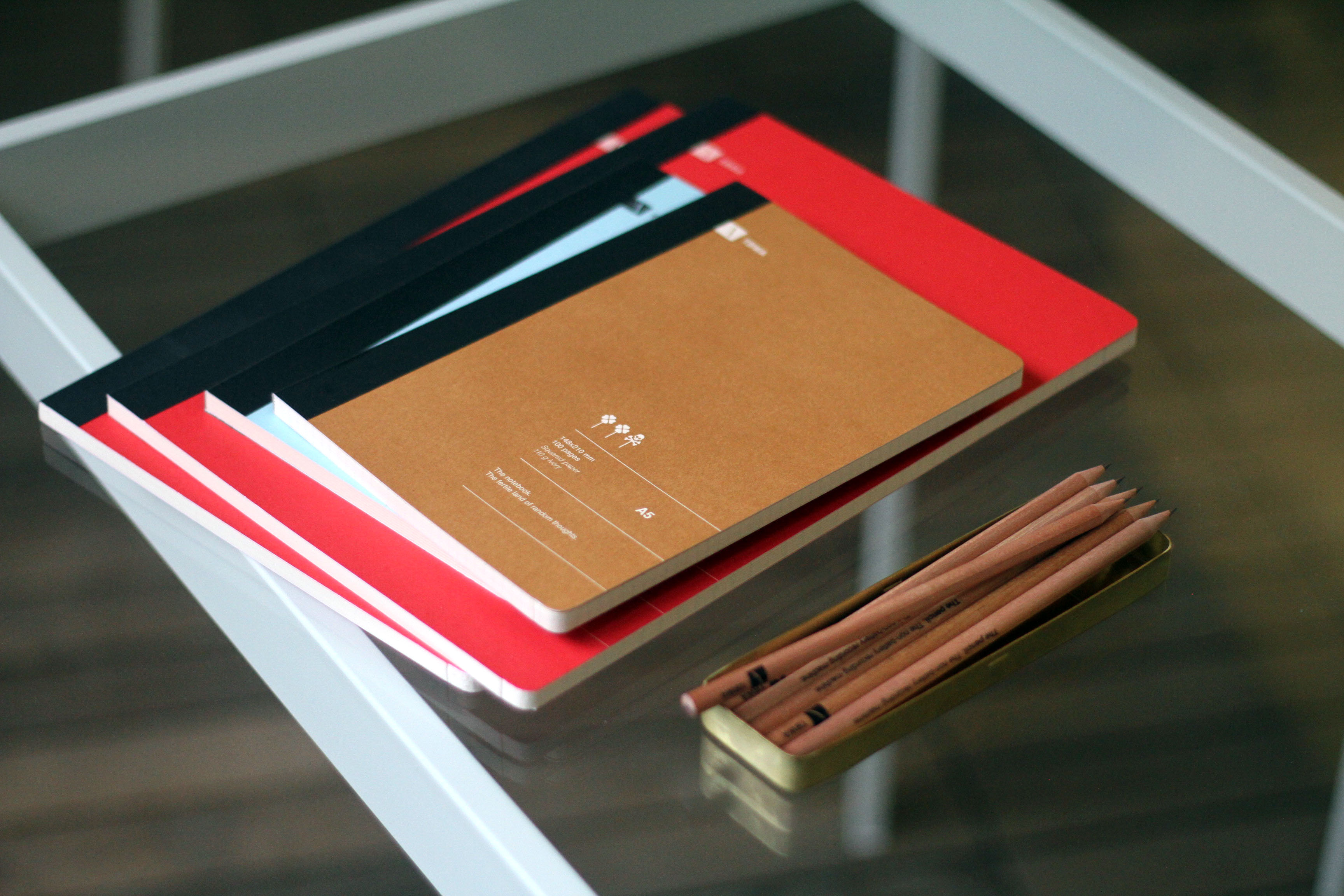 A photo of some red, cyan and brown notebooks and some crayons put in a metallic greenish box.