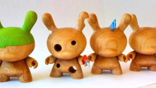 A group of wood sculptures figurines. One of them has green paint on its head. Another one has holes and what looks like an electric drill in its hand.