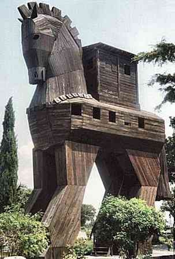 A photo of a wooden horse that might depict the trojan horse of old Greek stories. The horse is placed in a green park.