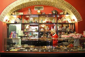 A photo of a woman working in an old cake shop and sitting near a display case.