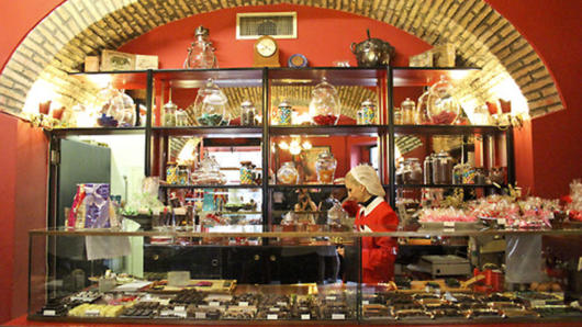 A photo of a woman working in an old cake shop and sitting near a display case.