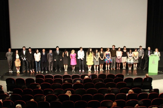 A photo of a group of people standing in line on the stage in front of audience.