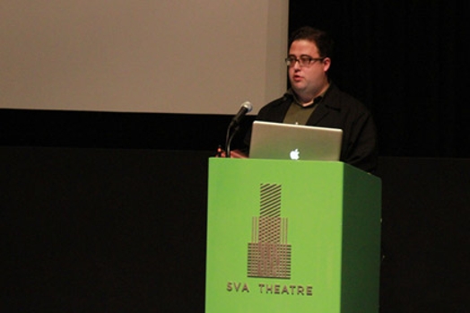 A photo of a man giving a lecture at a green stand with the text SVA Theatre on it.