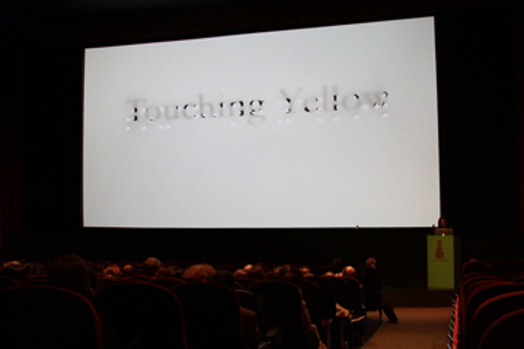 A photo of a screen projection showing a faded text that says: Touching Yellow.
