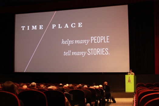 A photo of a screen projection showing the text Time Place helps many people tell many stories.