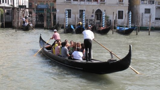A photo of a gondola in Venice with a group of people in it.