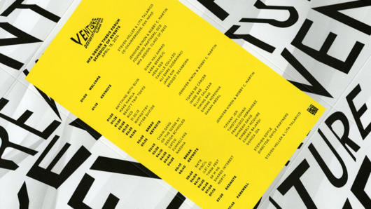 A yellow poster, placed on some black and white papers which has the entire Venture Design Entrepreneur schedule on it.