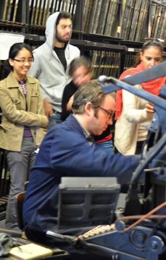 A photo of a man showing how a printing press works to a group of students.