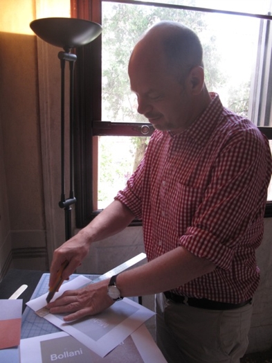 A photo of a man cutting some paper with an exactoknife and a ruler.