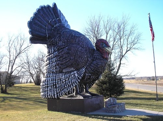 A sculpture or statue of a turkey put in a park near a stone bench.