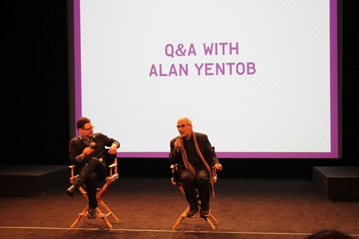 A photo of two people sitting on a stage in front of a screen projector with the text Q and A with Alan Yentob.