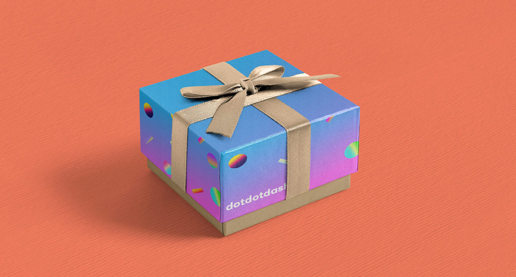 A photo of a present box, colored in blue pink gradient, with some other gradient colored circles on it. Also it has a golden gift wrap bow.