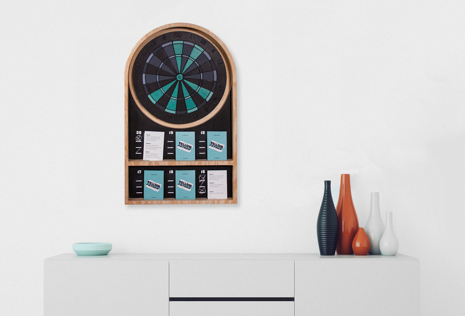 A photo of a darts game with cards and scoreboard, placed near a white cabinet that has on it a green ashtray and some black, red and white bottles.