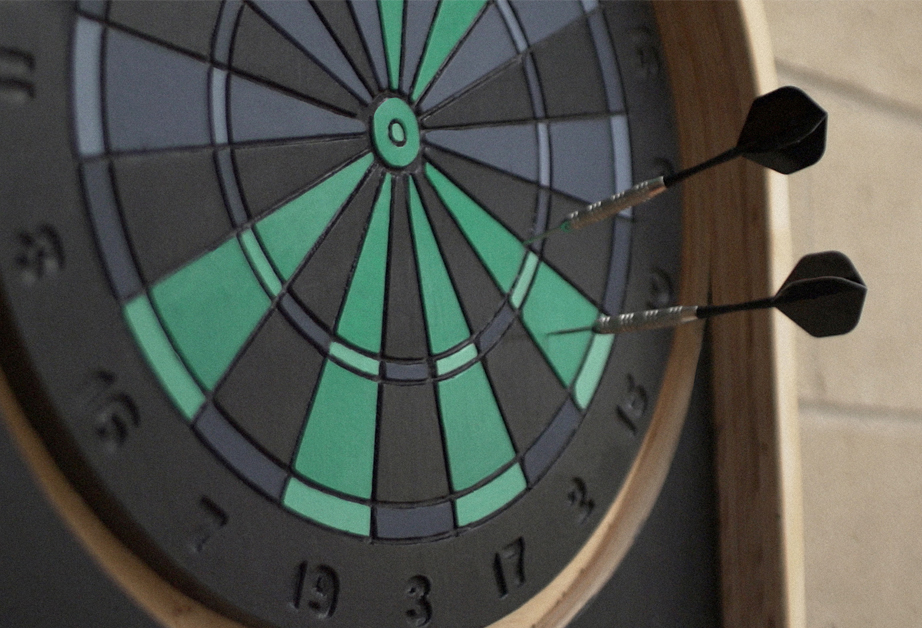 A photo of a grey, blue and green darts target and a few darts arrows in it.