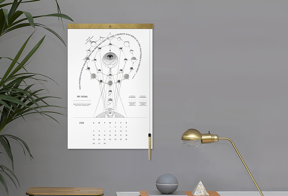A set of different gold plated objects like: a lamp, a white pyramid shape and a calendar with a drawing of different phases of the moon. Also there is a green plant and some grey ball on the table.