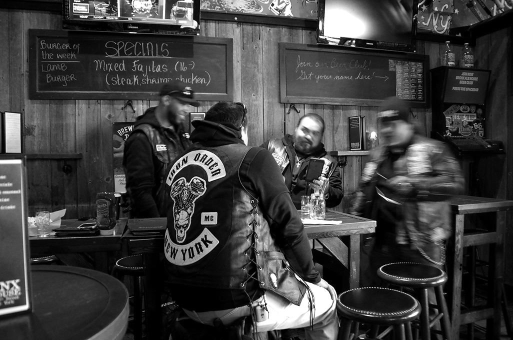 A black and white photo form a bar showing some bikers sitting at a table.