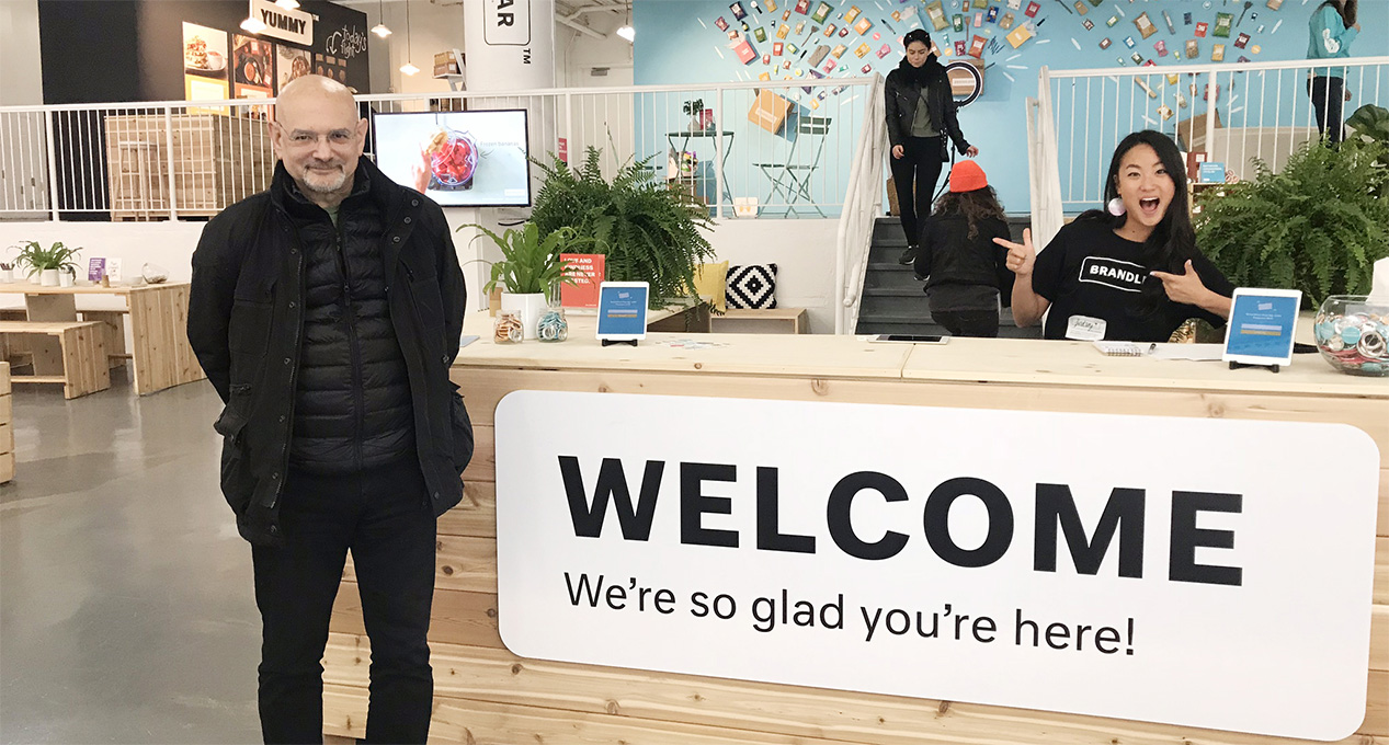 There is a front desk with a receptionist and a person standing near the reception area. The reception has the welcome message "welcome. We're so glad you are here!"