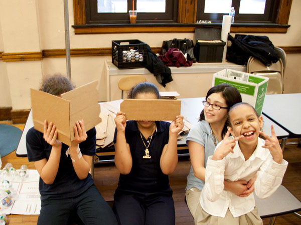 a group photo of four children, two hugging another two covering their faces with cardboards