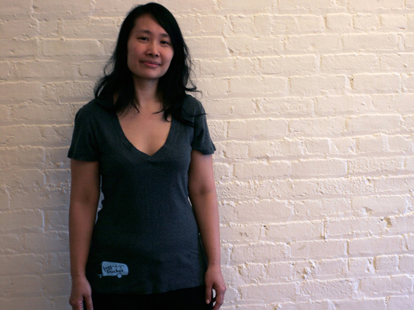 portrait of a woman wearing a black fuzz bucket t-shirt against a wall