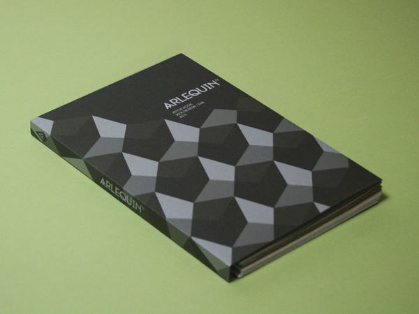 Arlequin book with black and grey polygonal shapes on the cover, and the book is on a green table