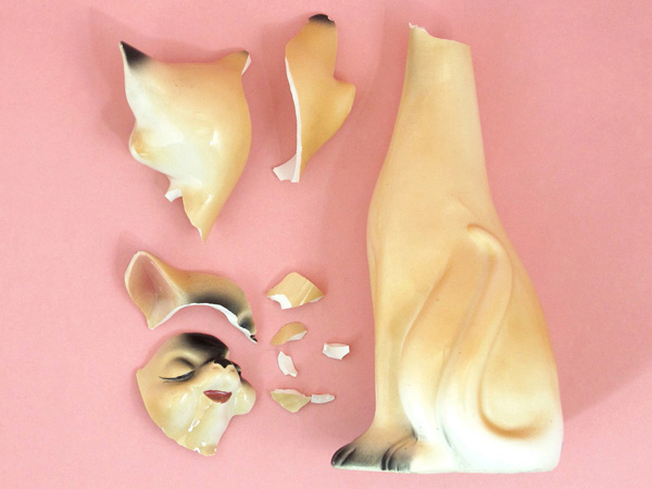 a porcelain cat sculpture broken into pieces is laid on a pink surface