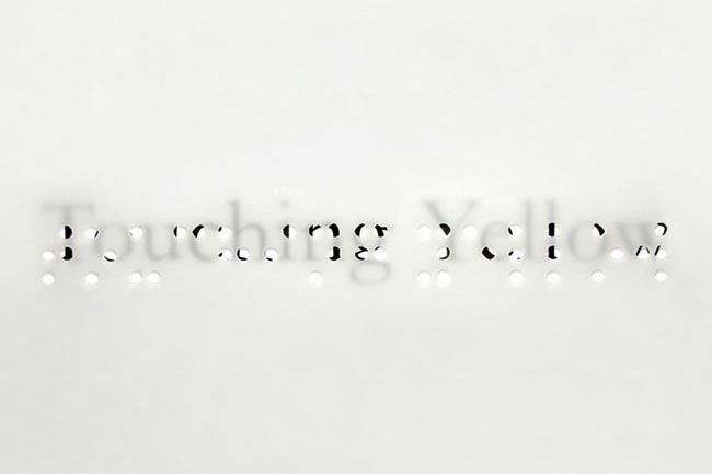 touching yellow word written on a piece of paper, an on top of it is placed a transparent foil with the two words written in braille