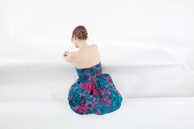photo of a woman wearing a blue dress sitting with the back to the camera in a white room