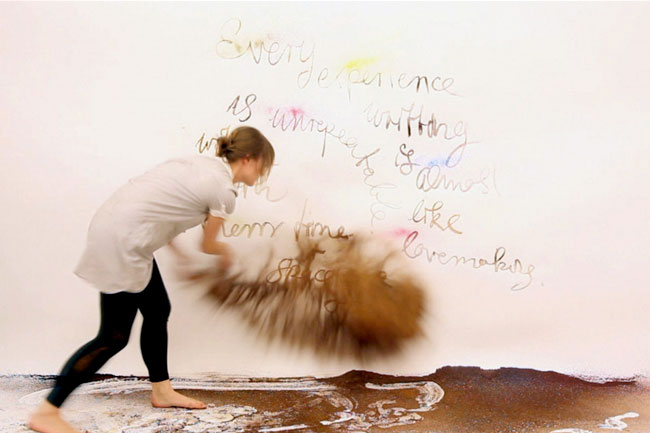 woman throwing brown powder to a white wall with text on it