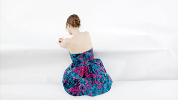 photo of a woman wearing a blue dress sitting with the back to the camera in a white room