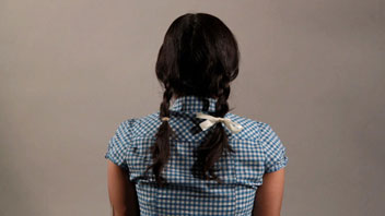 a girl sitting with hair braided in two tails sitting with the back to the camera