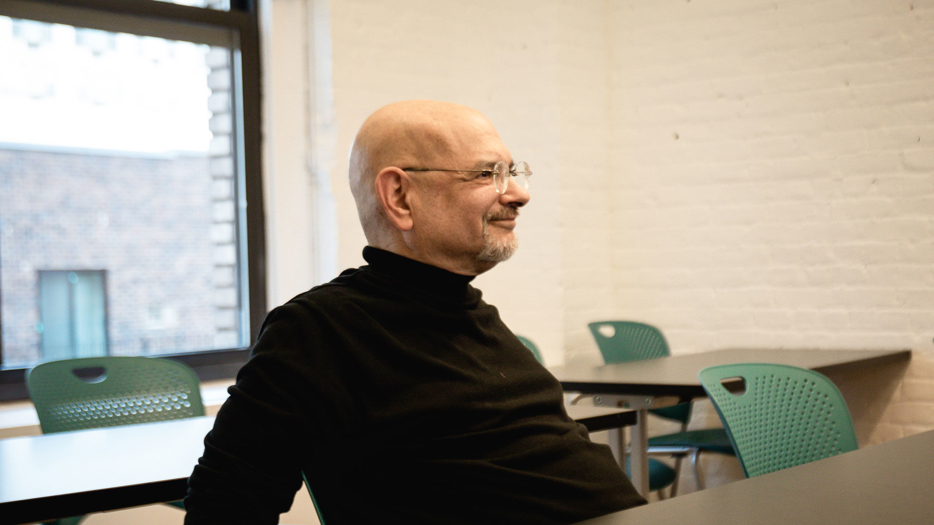 Steven Heller weaning glasses and black turtleneck, smiling in MFAD classroom