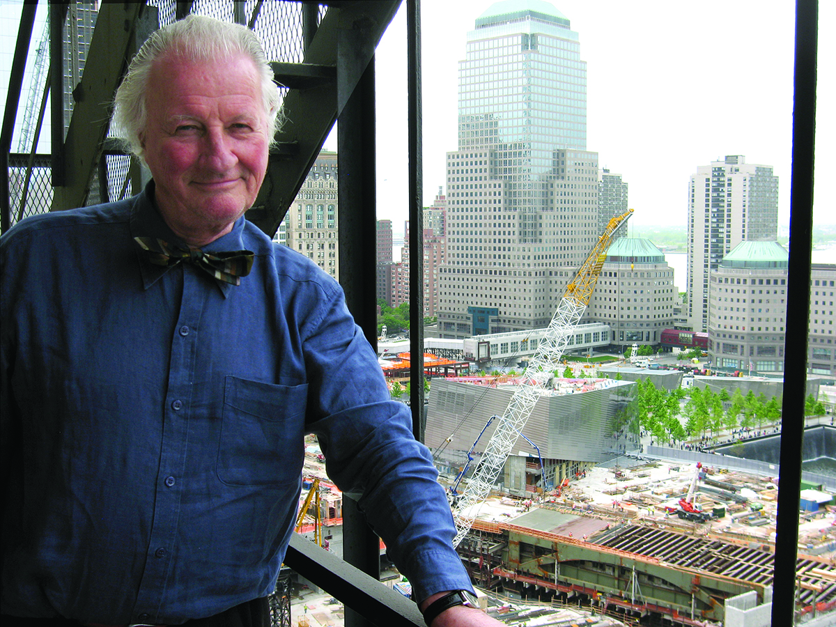 portrait of Keith Goddard in a blue shirt and brown bow, on a high-rise overlooking the city