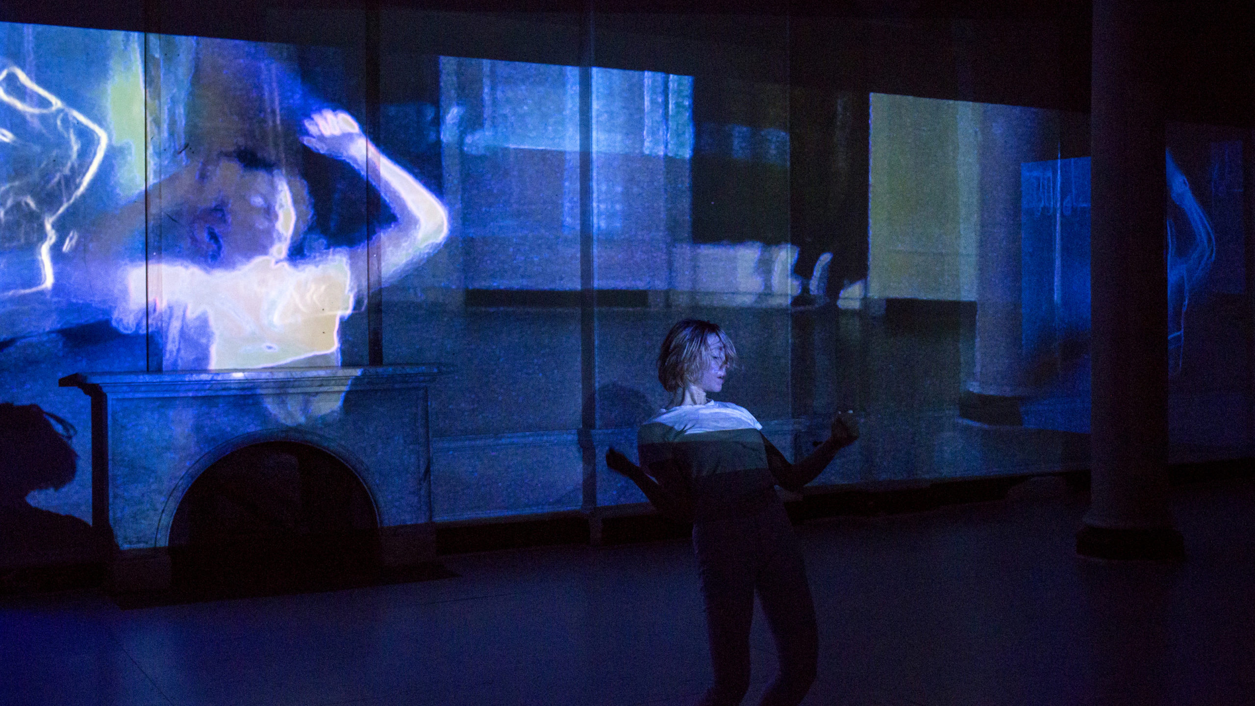 woman standing and leaning backwards on a stage in front of a blue projection of a woman