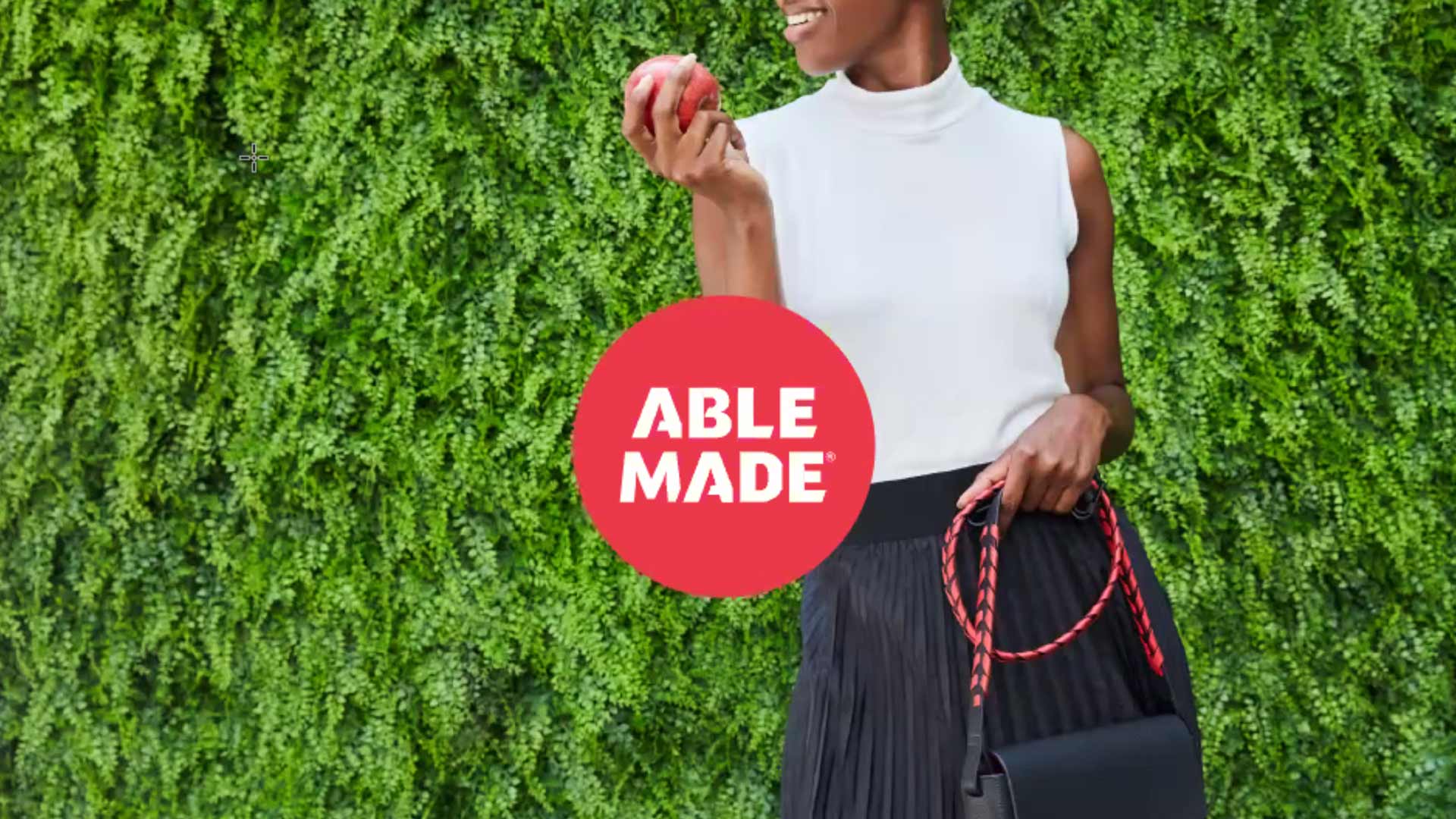 woman with white top and black skirt eating an apple and holding a purse words able made in center of red circle