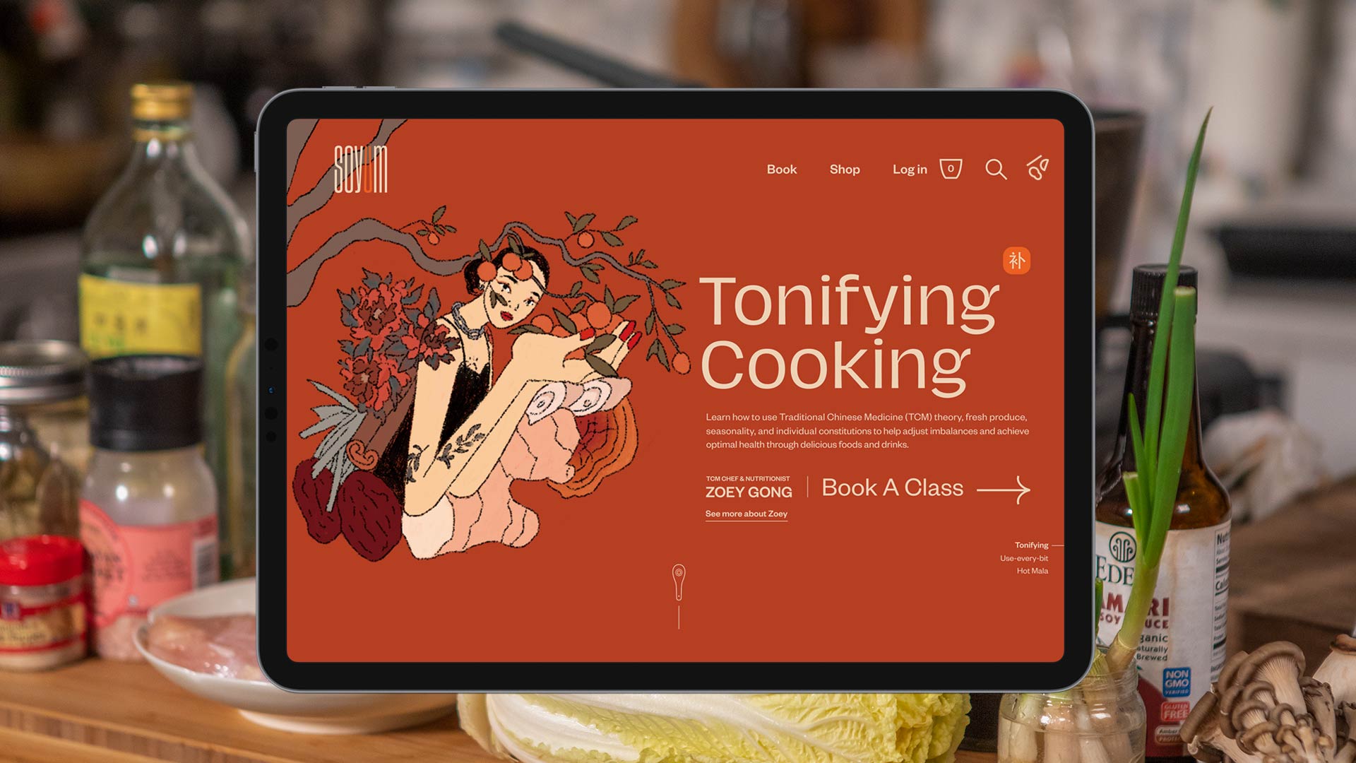 An iPad view showing Soyum website homepage against a kitchen background with Asian ingredients and condiments on the table