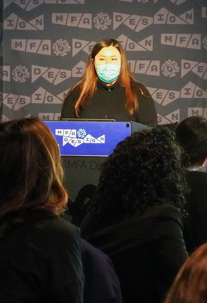 Close portrait of a woman with a face mask, long hair, and a black blouse giving a speech
