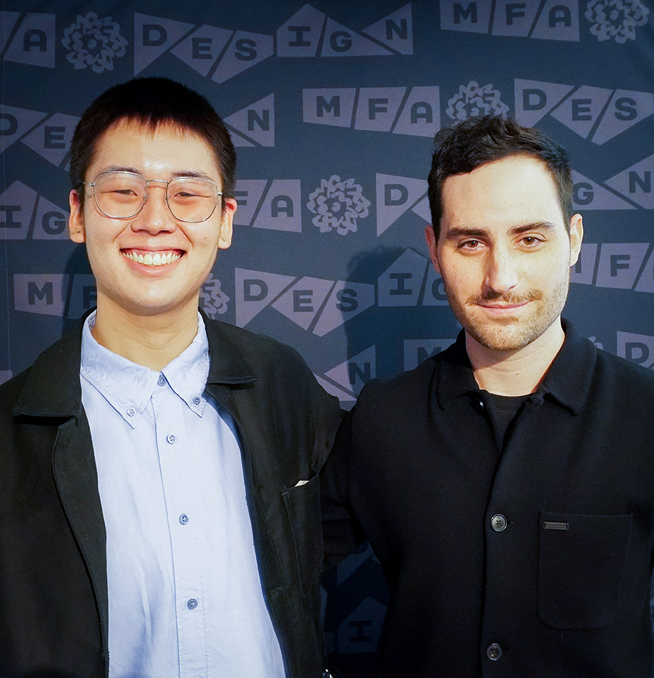 Portrait of two-man with black coats and one has a light blue shirt under the coat, in front of an MFA Design navy blue backdrop