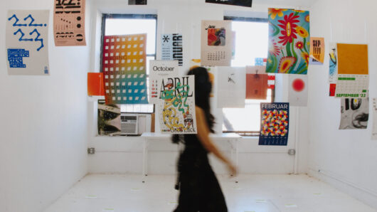 Exhibition with multiple multi-colored posters hanging from the ceiling and a person crossing the room