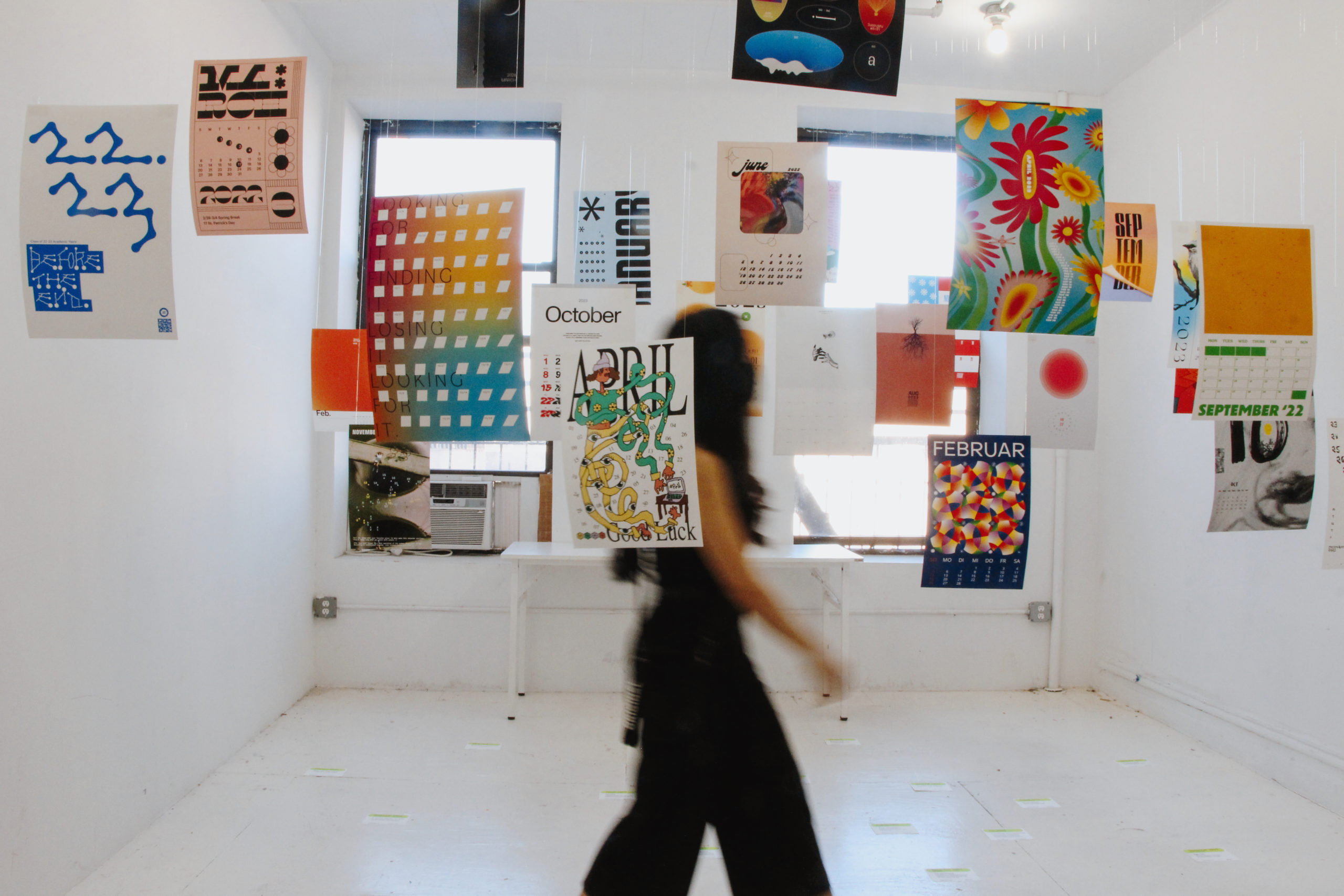 Exhibition with multiple multi-colored posters hanging from the ceiling and a person crossing the room