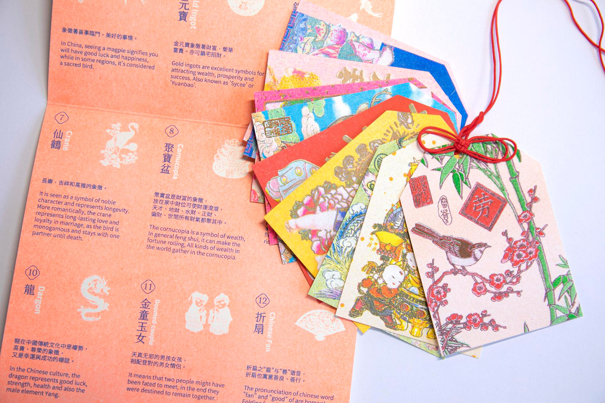 A set colorful cloth labels tied together by a red string. There is also an unfolded orange card with different pictograms and Asian text.